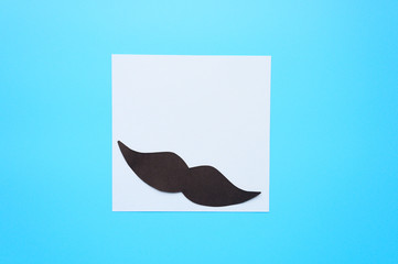 Black paper moustache and writing paper sticker on a blue background. The concept of awareness of...
