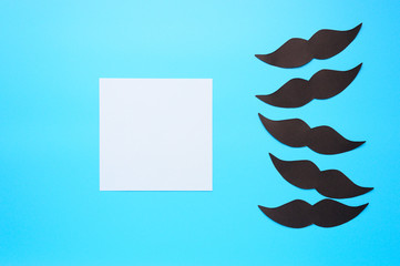 Several black paper moustache and writing paper sticker on a blue background. The concept of...