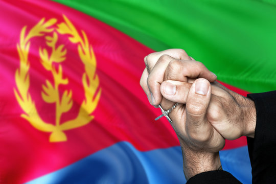 Eritrea flag and praying patriot man with crossed hands. Holding cross, hoping and wishing.