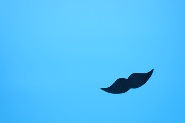 Black paper moustache on a blue background. The concept of awareness of men's health and prostate...