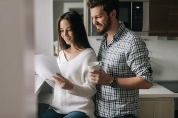 Portrait of young happy couple is reading documents. Daily life of a male and female in apartment.