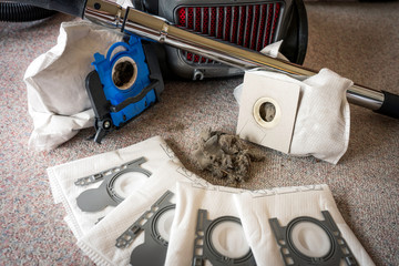 Vacum cleaner sitting on the floor with new and old dust bags and dust particles in the middle....