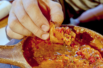 Fingers hold a piece of bread dipped in meat sauce, close-up