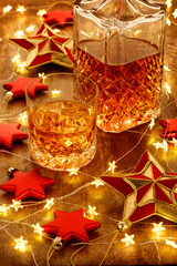 Crystal glass of whisky and a whisky decanter with christmas lights, baubles and red stars decorations