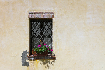 Window in Tuscany with yellow wall and pink flowers. Sun, shadows, italy, travel, house, home, rustic concept.