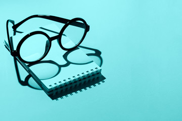 black round glasses lie on a Notepad and cast shadow on the mint background