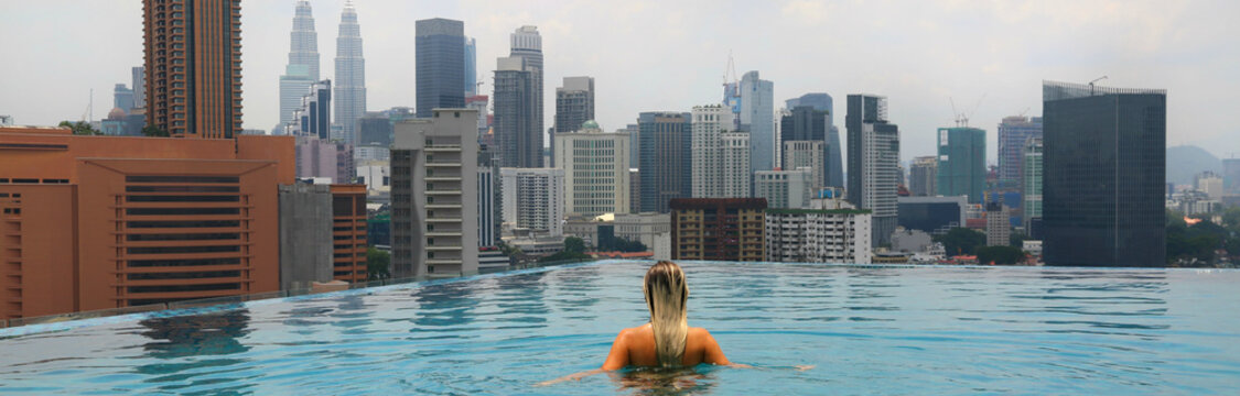 Young happy girl swimming alone in the infinity pool on rooftop in Kuala Lumpur in Malaysia. Horizontal photo.