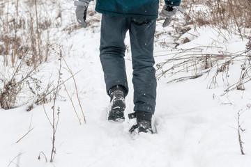 The boy walks in the snow, field, meadow, dead wood. Warm jacket, warm pants, winter gloves.