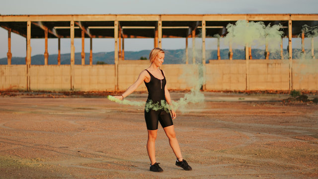 happy young woman having fun with colorful powder cloud. girl running with yellow color smoke bomb