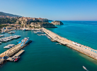 Fototapeta na wymiar Aerial view of boats moored at the Port of Tropea, Calabria, Italy. Houses overlooking the sea. Beach and Sanctuary on the horizon. Italian coasts
