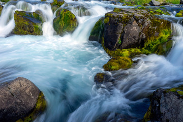 Waterfalls with clear blue water and green mossy boulders outdoors in the icelandic nature.