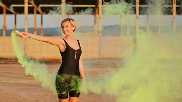 happy young woman having fun with colorful powder cloud. girl running with yellow color smoke bomb