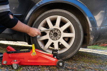 Using wrench on tire bolt infront of red garage if. Changing tire.