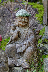 Old stone statue of Buddhist monk wearing knitted hat with book in his hands.