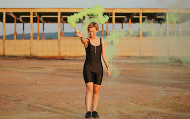 Naklejka premium happy young woman having fun with colorful powder cloud. girl running with yellow color smoke bomb