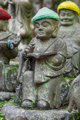 Old stone statue of Buddhist monk wearing knitted hat with book in his hands.