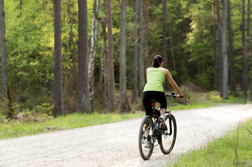 Fototapeta premium Back view of woman riding bike on path in forest. She exploring with joy.