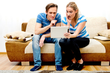 Couple sitting on sofa and watching movie on tablet. Streaming media on internet.