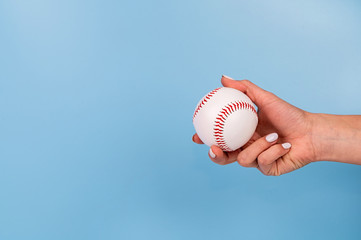 Female hand with white nails holding white baseball on blue background