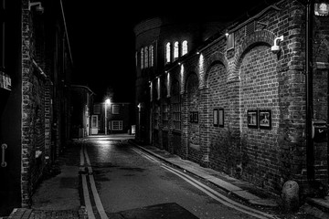 dark street in old city between buildings made of bricks and with light in the end in black and white
