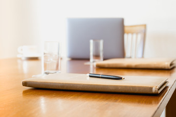 Pen on folder with glass of water and laptop on meeting desk.
