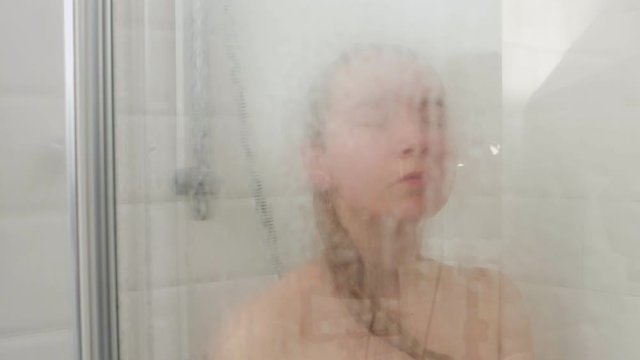 Woman taking shower behind glass curtain. She enjoying under shower.