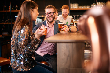 Small group of friends sitting in irish pub at bar counter, drinking beer and chatting. Nightlife.