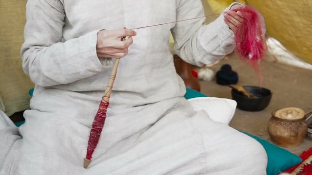 Woman in medieval cotton dress spinning with a wheel. Lady makes yarn from a sheep's wool. Hand spindles. Spinning Wheel. Spinning yarn. Process twisting fibers wool, flax, hemp, cotton into yarn