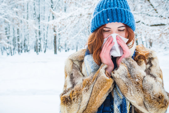 portrait of a young woman in the winter forest. a beautiful girl sneezes into a napkin. get sick in winter.