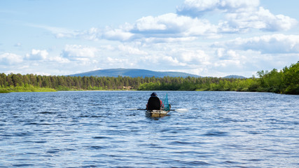 Man fishing on a kayak on the river with clear blue water. Fisherman kayaking in the river. Leisure activities on water. Fishing in Lapland.