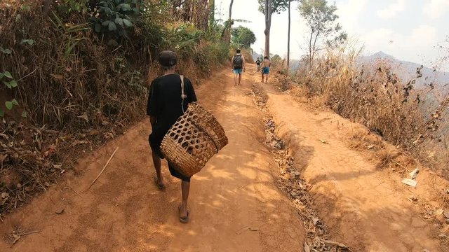 Old Asian Man with Empty Basket Walking on a Small Road in the Mountains in Thailand, with other People in Background