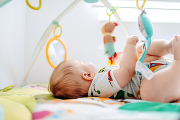 Adorable six months old boy lying in bed and playing with crib toys. Healthy upbringing concept.