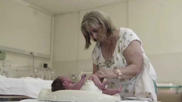 Senior nurse changing diapers newborn baby at maternity ward.