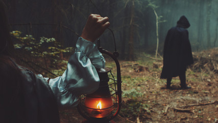 Girl with lantern and among male figure in the terrible forest. Wonderful scene for Halloween © procinemastock