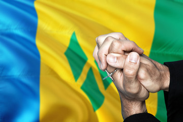 Saint Vincent And The Grenadines flag and praying patriot man with crossed hands. Holding cross,...