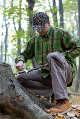 Fototapeta premium Man with knife sharpening a wooden stick for campfire in the forest. Bushcraft, hunting and people concept. - Image
