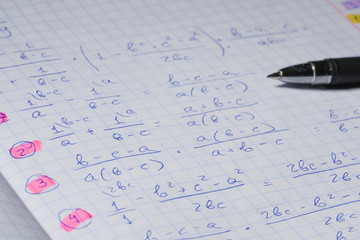 Algebraic calculations in open graph notebook with black pen. White paper with math fractions