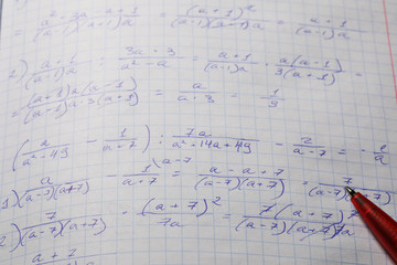 Algebraic calculations in open graph notebook with red pen. White paper with math fractions
