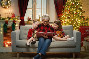 Fototapeta Grandmother reading  to granddaughters near Christmas tree. obraz