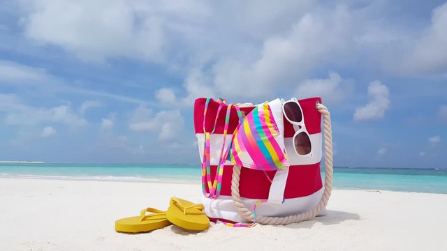 Summer set bag of woman with bikini, sunglasses and flip flops left over white sand, colorful copy space