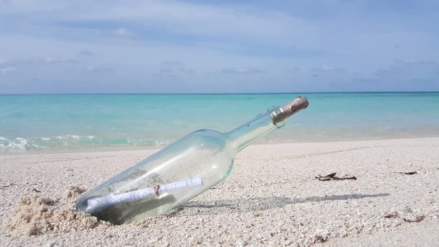Message in a bottle plunged on white sand of an empty beach with blur ocean background in Bali, copy space