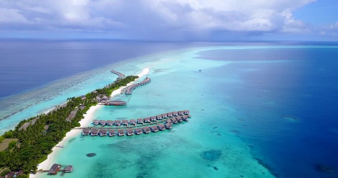 Row of luxurious bungalows built on shallow turquoise waters of tiny island in Caribbean