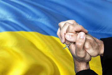 Ukraine flag and praying patriot man with crossed hands. Holding cross, hoping and wishing.