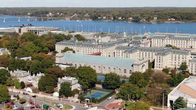 Aerial pan reveals US Naval Academy grounds, buildings, playing fields, blue Severn River, sunny day
