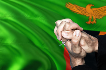 Zambia flag and praying patriot man with crossed hands. Holding cross, hoping and wishing.