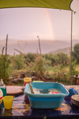 Doing the dishes on a remote camp site with view on mountains with a rainbow.