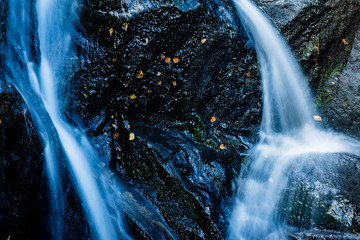 close up shot of a waterfall in the argyll region of the highlands of scotland in autumn showing bright water flowing over dark black rock