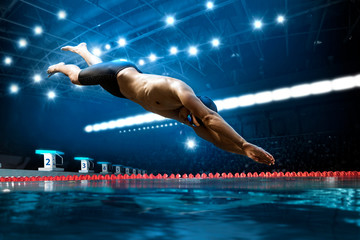 Swimmer jumping from starting block in a swimming pool