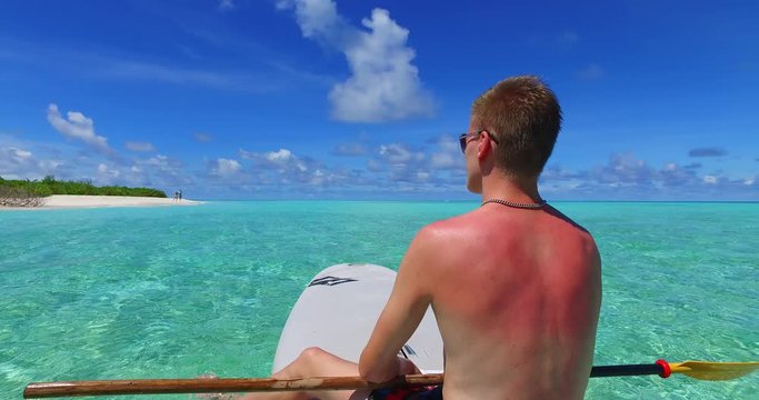 tropical vacation establishing, opening shot. Young handsome man with a sunburn on the back, relaxing on the paddleboard in the turquoise crystal clear seawater, Maldives