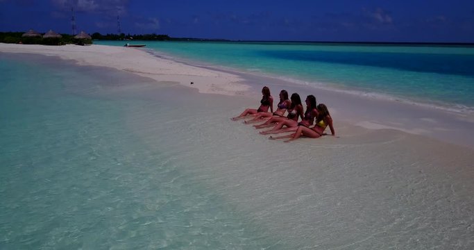 five sexy girls sitting and sunbathing on the white sand sanbar. tropical sea water reaches their feet